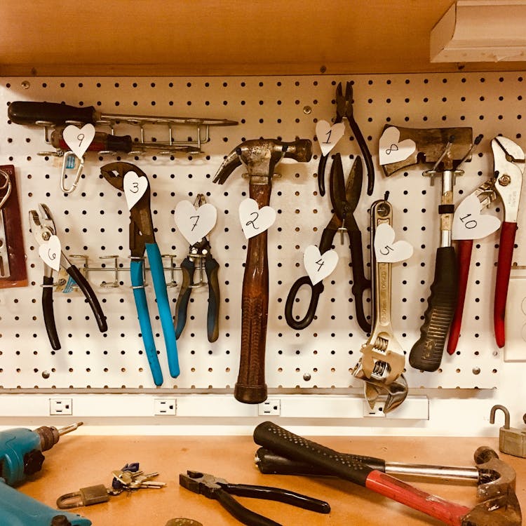 Hand tools including hammers, pliers, and wrenches hung on a white pegboard in a home workshop
